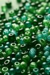 DALL·E 2024-05-21 20.47.10 – A detailed close-up of a variety of green seed beads. The beads are small, uniformly round, and made of glass. They shine brightly, reflecting the lig